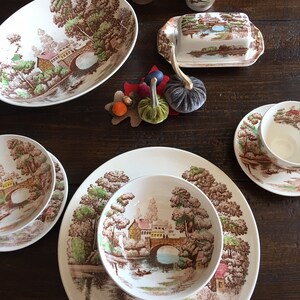 Puede incluir: Un juego de platos de cer&aacute;mica vintage marr&oacute;n y blanco con un dise&ntilde;o cottagecore que presenta un puente, &aacute;rboles y un r&iacute;o. Los platos incluyen un taz&oacute;n ovalado grande para servir, un taz&oacute;n m&aacute;s peque&ntilde;o, un plato y una mantequillera.