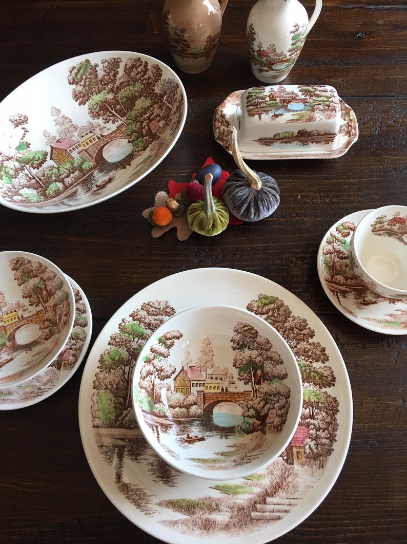 Puede incluir: Un juego de platos de cer&aacute;mica vintage marr&oacute;n y blanco con un dise&ntilde;o cottagecore que presenta un puente, &aacute;rboles y un r&iacute;o. Los platos incluyen un taz&oacute;n ovalado grande para servir, un taz&oacute;n m&aacute;s peque&ntilde;o, un plato y una mantequillera.