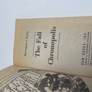 May include: The cover of a paperback book titled "The Fall of Chronopolis" by Barrington J. Bayley. The book is published by DAW Books, Inc. and features a black and white illustration of a futuristic city.