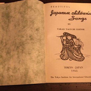May include: The cover of a book titled "Beautiful Japanese Children's Songs" by Takao Taguchi Editor. The book cover features a black and white illustration of a child wearing a traditional Japanese outfit and holding a branch. The book was published in Tokyo, Japan in 1963 by The Tokyo Institute for International Education Research.