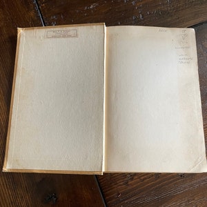 May include: An open book with aged, off-white pages. The left page has a printed label with text. The right page has handwritten notes including "ARCH", "OP 1500", and "bluebook". The book's cover is a light tan color.