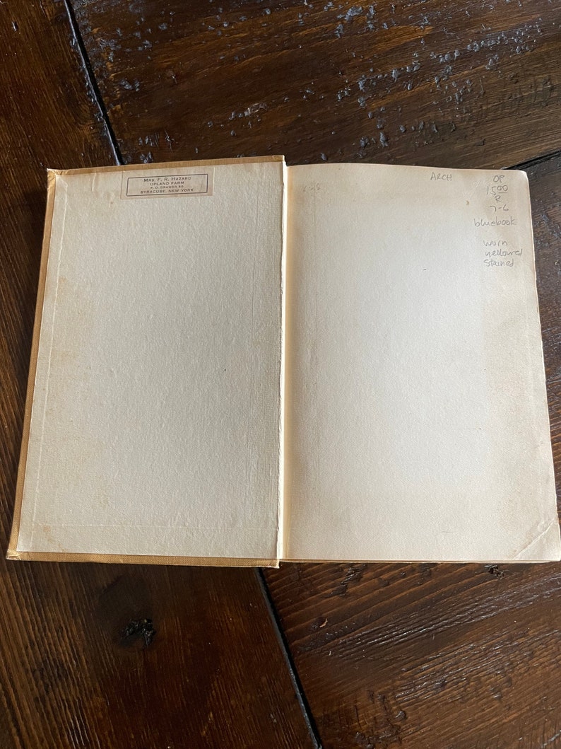 May include: An open book with aged, off-white pages. The left page has a printed label with text. The right page has handwritten notes including "ARCH", "OP 1500", and "bluebook". The book's cover is a light tan color.