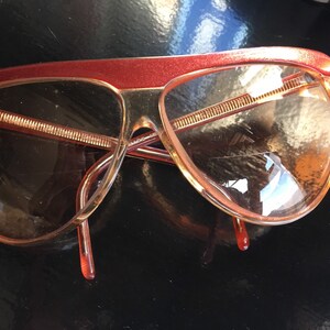 May include: A pair of red and brown plastic sunglasses with a curved frame and brown lenses.