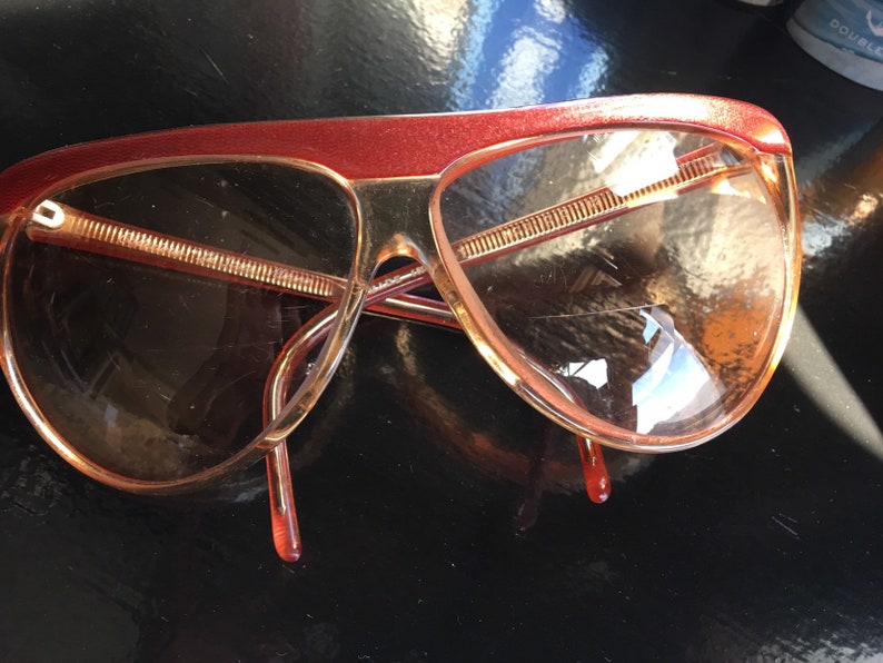 May include: A pair of red and brown plastic sunglasses with a curved frame and brown lenses.