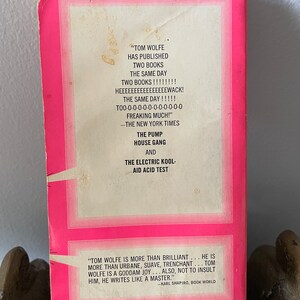 May include: A pink book cover with white text. The text reads "TOM WOLFE HAS PUBLISHED TWO BOOKS THE SAME DAY TWO BOOKS!!!!!!! HEEEEEEEEEEEEEEEWACK! THE SAME DAY!!!!! T00-0-0-0-0-0-0-0-0-0-0-0 FREAKING MUCH!" -THE NEW YORK TIMES THE PUMP HOUSE GANG AND THE ELECTRIC KOOL-AID ACID TEST "TOM WOLFE IS MORE THAN BRILLIANT... HE IS MORE THAN URBANE, SUAVE, TRENCHANT... TOM WOLFE IS A GODDAM JOY... ALSO, NOT TO INSULT HIM, HE WRITES LIKE A MASTER." -KARL SHAPIRO, BOOK WORLD