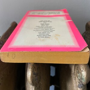 May include: Close-up of the spine of a pink paperback book with the text "TOM WOLFE HAS PUBLISHED TWO BOOKS THE SAME DAY" and "THE PUMP" printed on the spine.