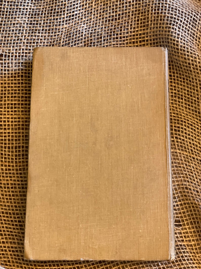 May include: A closed, rectangular book with a tan linen cover. The book's spine is visible on the right side, and the cover has a slightly textured appearance. The background is a woven, tan material.