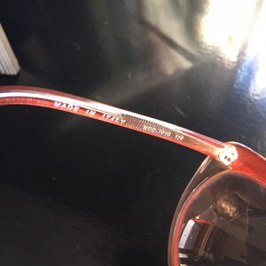 May include: Close-up of the inside of a pair of red sunglasses with the text "MADE IN ITALY MOD. 7010 112" printed on the arm.