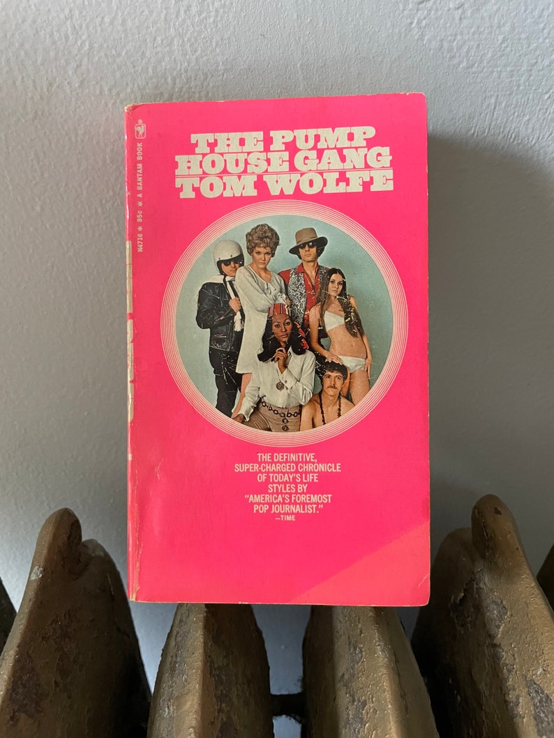 May include: A pink paperback book with a white circle on the cover. The circle contains a photo of six people. The book title is "The Pump House Gang" by Tom Wolfe. The text below the title reads "The definitive, super-charged chronicle of today's life styles by "America's foremost pop journalist." -TIME"