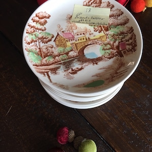 Puede incluir: Una pila de platos de pan y mantequilla de 15,24 cm de di&aacute;metro con un dise&ntilde;o floral marr&oacute;n y blanco que presenta un puente y una casa. Los platos est&aacute;n etiquetados con "6" Bread + butter plates, Nasco Town Holiday" en una nota adhesiva amarilla.