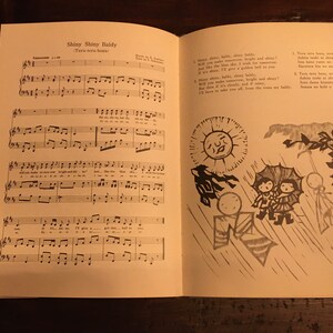 May include: A vintage sheet music book with a black and white illustration of a sun, rain, and people with umbrellas. The sheet music is for a song called "Shiny Shiny Baldy (Terr-terr-terr beat)".