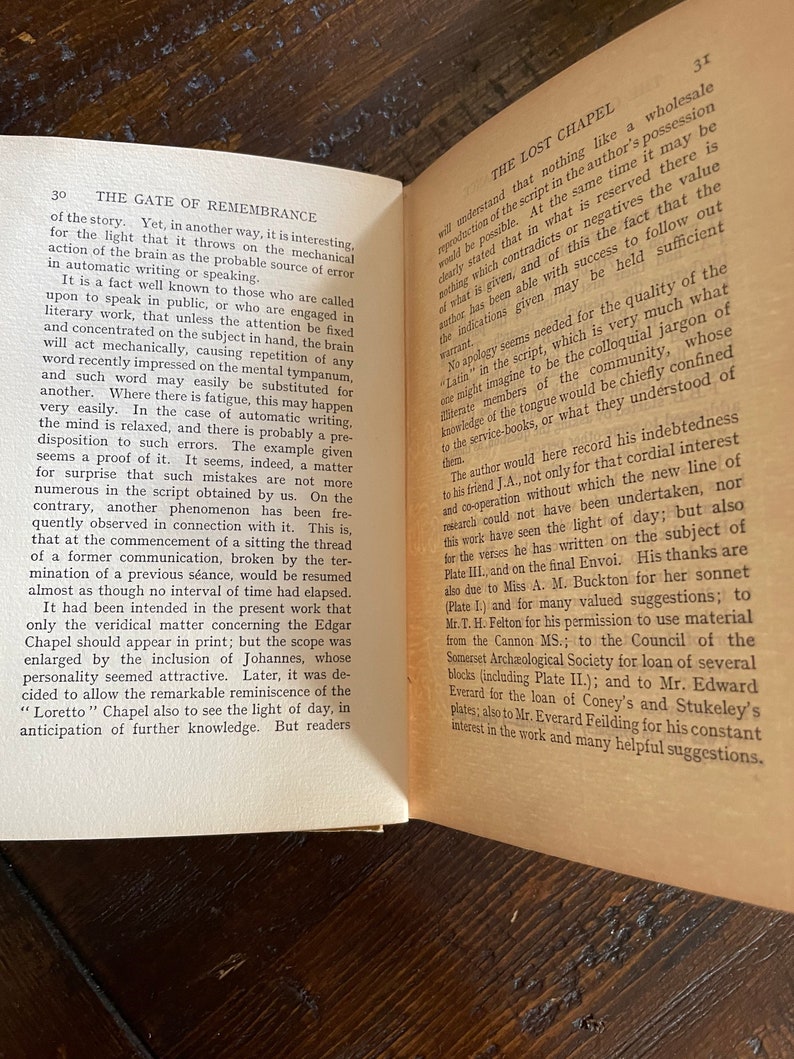 May include: Open book with text on aged paper. The left page has a section titled "THE GATE OF REMEMBRANCE." The right page is titled "THE LOST CHAPEL." The pages are slightly yellowed, suggesting age. The book is open on a wooden surface.