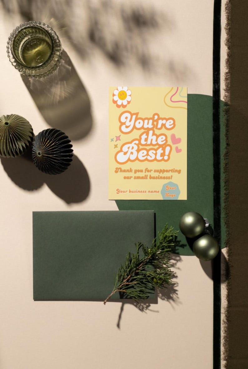 Puede incluir: Una tarjeta de agradecimiento amarilla con el texto "You're the Best!" en una fuente retro. La tarjeta tiene una margarita, corazones y remolinos de colores arco&iacute;ris. El texto "Thank you for supporting our small business!" est&aacute; debajo del texto principal. La tarjeta est&aacute; sobre una superficie beige con adornos verdes y un sobre verde.