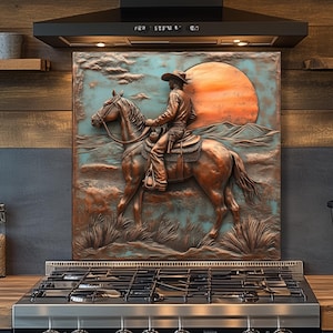 May include: A copper-toned relief sculpture of a cowboy on horseback against a sunset backdrop. The artwork, with a turquoise and orange color palette, is mounted above a stainless steel gas range in a kitchen setting. The cowboy wears a hat and leather attire.