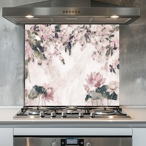 Puede incluir: Una placa protectora de cocina decorativa con un diseño floral de flores de loto rosas, hojas verdes y delicadas flores rosas. El fondo tiene una textura similar al mármol. La placa se instala sobre una encimera de gas.