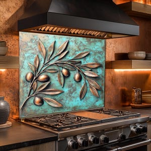 Pu&ograve; includere: Un paraschizzi da cucina con un design a ramo d'ulivo in bronzo su uno sfondo turchese e strutturato. L'immagine mostra un piano cottura a gas in acciaio inossidabile e una cappa nera. Il tema generale &egrave; l'arredamento della cucina.