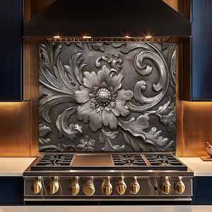 May include: A decorative kitchen backsplash with a large, detailed floral design in a metallic silver finish. The design features a central flower surrounded by leaves and swirling patterns. The backsplash is installed above a stainless steel gas range with gold knobs.