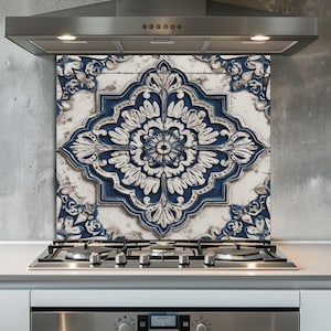 Pode incluir: Um painel de cozinha decorativo com um grande e ornamentado design floral azul e branco. O azulejo é colocado sobre um fundo neutro e é instalado acima de um fogão a gás e uma exaustor em aço inoxidável.