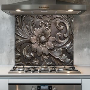 May include: A decorative kitchen backsplash with a detailed floral design in shades of silver and gray. The embossed pattern features a large central flower surrounded by leaves and swirling accents. The backsplash is installed above a gas stovetop.