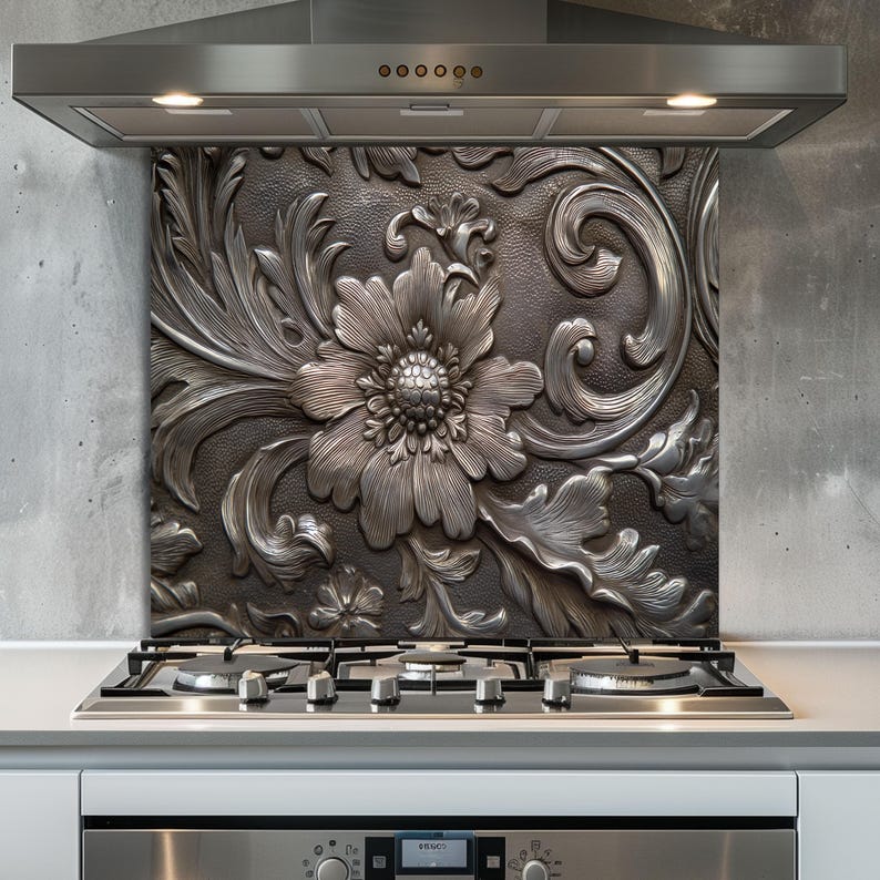May include: A decorative kitchen backsplash with a detailed floral design in shades of silver and gray. The embossed pattern features a large central flower surrounded by leaves and swirling accents. The backsplash is installed above a gas stovetop.
