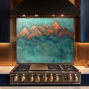 Op de afbeelding: Een keukenachterwand met een bergketenontwerp in tinten turquoise en koper. Daarboven een roestvrijstalen gasfornuis met goudkleurige knoppen. De keuken heeft donkerblauwe kasten en een zwarte afzuigkap.