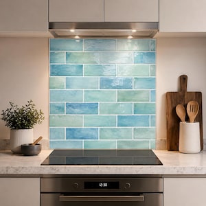 May include: A kitchen splashback featuring rectangular subway tiles in varying shades of blue and green with a glossy finish. The tiles are arranged in a horizontal brick pattern behind a black glass hob and a stainless steel oven.