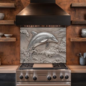 May include: A stainless steel kitchen backsplash features a detailed, three-dimensional relief of a dolphin leaping from ocean waves. The dolphin is silver, and the waves are textured. The backsplash is mounted above a stainless steel gas range.