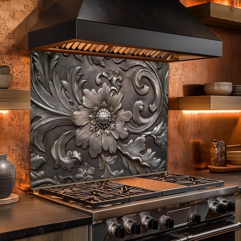 May include: A kitchen backsplash with a large, ornate floral design in shades of silver and gray. The backsplash is installed behind a stainless steel gas range and beneath a black range hood. The kitchen has wooden shelves and copper-toned walls.