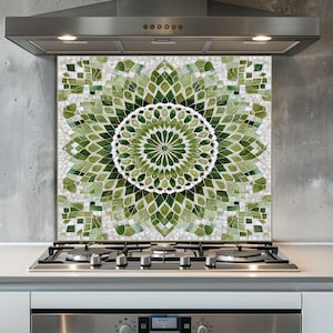May include: A decorative kitchen backsplash featuring a mosaic design with shades of green and white. The mosaic forms a floral pattern, with a central white circular design. The backsplash is installed above a gas stove and below a stainless steel range hood.