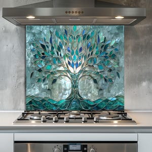Puede incluir: Un protector contra salpicaduras de cocina con un diseño de árbol estilo vidriera. El árbol tiene un tronco y ramas con hojas en tonos azules y verdes. El fondo es un mosaico de baldosas azul claro y grises. El protector está montado sobre una encimera de gas.