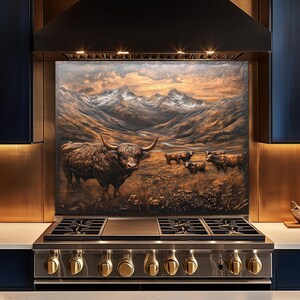 Puede incluir: Un protector contra salpicaduras de cocina con una vaca de las Highlands en un paisaje monta&ntilde;oso. La obra de arte est&aacute; en tonos marrones, dorados y grises, con una cocina de gas de acero inoxidable debajo. La escena incluye varias vacas y una puesta de sol.