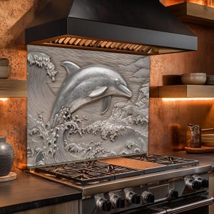May include: A stainless steel kitchen backsplash featuring a detailed relief of a dolphin leaping from ocean waves. The artwork is set above a gas range and below a black range hood, adding a nautical theme to the kitchen.