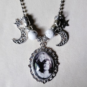 May include: A silver necklace featuring a pendant with a black and white photo of two people. The necklace has decorative crescent moons and star charms, along with white and gray marbled beads. The chain is a delicate silver color.