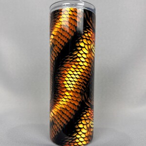 May include: A stainless steel tumbler with a black and gold snake skin pattern. The tumbler has a clear lid.