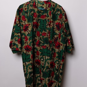 May include: A short-sleeved shirt with a vibrant floral pattern in green, red, and gold. The shirt is hanging on a blue hanger against a white background. The fabric features a repeating design of stylized flowers and leaves.