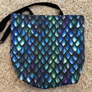 Könnte beinhalten: Eine blaue und grüne Einkaufstasche mit einem Drachenschuppenmuster. Die Tasche hat schwarze Henkel.