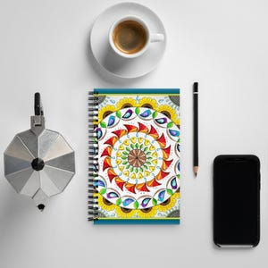 May include: A spiral bound notebook with a colorful mandala design featuring sunflowers, birds, and teardrop shapes. The cover is a vibrant mix of yellow, red, blue, and green.
