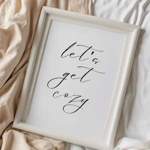 May include: White framed print with the words "let's get cozy" in elegant black script. The artwork is displayed on a white background, creating a minimalist aesthetic. The frame is a simple, clean design.