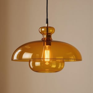 May include: Amber-colored glass pendant light fixture. The light has a domed shade and a smaller, bowl-shaped lower section. A vintage-style light bulb is visible inside. The fixture hangs from a black cord.