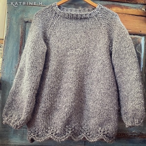 May include: A gray knitted sweater with a scalloped hem. The sweater has a round neckline and long sleeves.