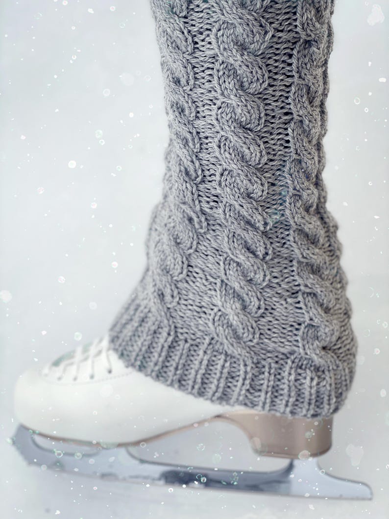 May include: Gray knitted leg warmers with a cable knit pattern, worn over white ice skates.