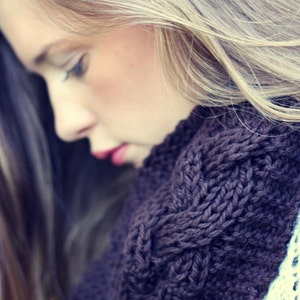 May include: A close-up of a woman with long, blonde hair wearing a dark brown knitted scarf. The scarf has a cable knit pattern and is worn around the neck.