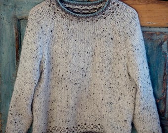 May include: A white sweater with a speckled pattern and a blue and brown trim around the neck and hem.