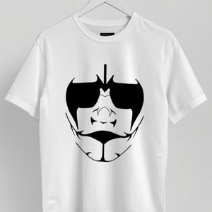 May include: White t-shirt featuring a black graphic design of a stylized face with sunglasses. The design includes a nose, mustache, and a pointed chin. The t-shirt is hanging on a white hanger.