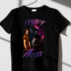 Puede incluir: Camiseta negra con un diseño gráfico que presenta varias figuras con maquillaje y ropa oscura. Las palabras "FRYBOY" y "Archer" están escritas en una fuente estilizada. El diseño incorpora un degradado de color púrpura y rosa.