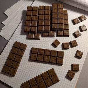 Pode incluir: Várias barras de chocolate castanho e peças quadradas individuais dispostas numa superfície. Cada barra e peça apresenta um padrão de grelha de pequenos retângulos com linhas verticais e horizontais alternadas em relevo.