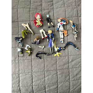 May include: A collection of disassembled anime figurines, featuring various characters in different poses and outfits. The figures are in various states of assembly, with detached limbs and accessories scattered across a gray surface.