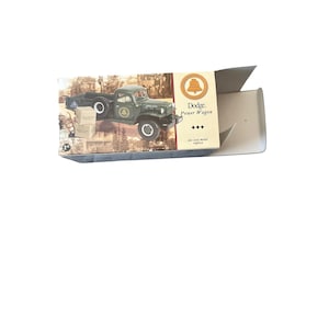 May include: A die-cast metal replica of a green Dodge Power Wagon truck is displayed inside its original box. The box features an image of the truck and the words "Dodge Power Wagon". The truck has white tires and a detailed design.