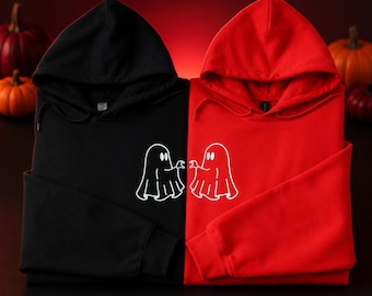 Könnte beinhalten: Ein schwarzer Kapuzenpullover und ein roter Kapuzenpullover nebeneinander. Jeder Kapuzenpullover zeigt eine weiße Strichgrafik eines Geistes, wobei die beiden Geister so positioniert sind, dass ihre Hände in der Mitte zueinander zu reichen scheinen.