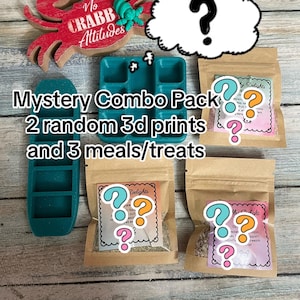 May include: A mystery combo pack featuring two teal 3D-printed plastic trays, three small brown paper pouches with labels, and a red wooden crab cutout with the text No CRABB Attitudes. The text Mystery Combo Pack 2 random 3d prints and 3 meals/treats is visible.